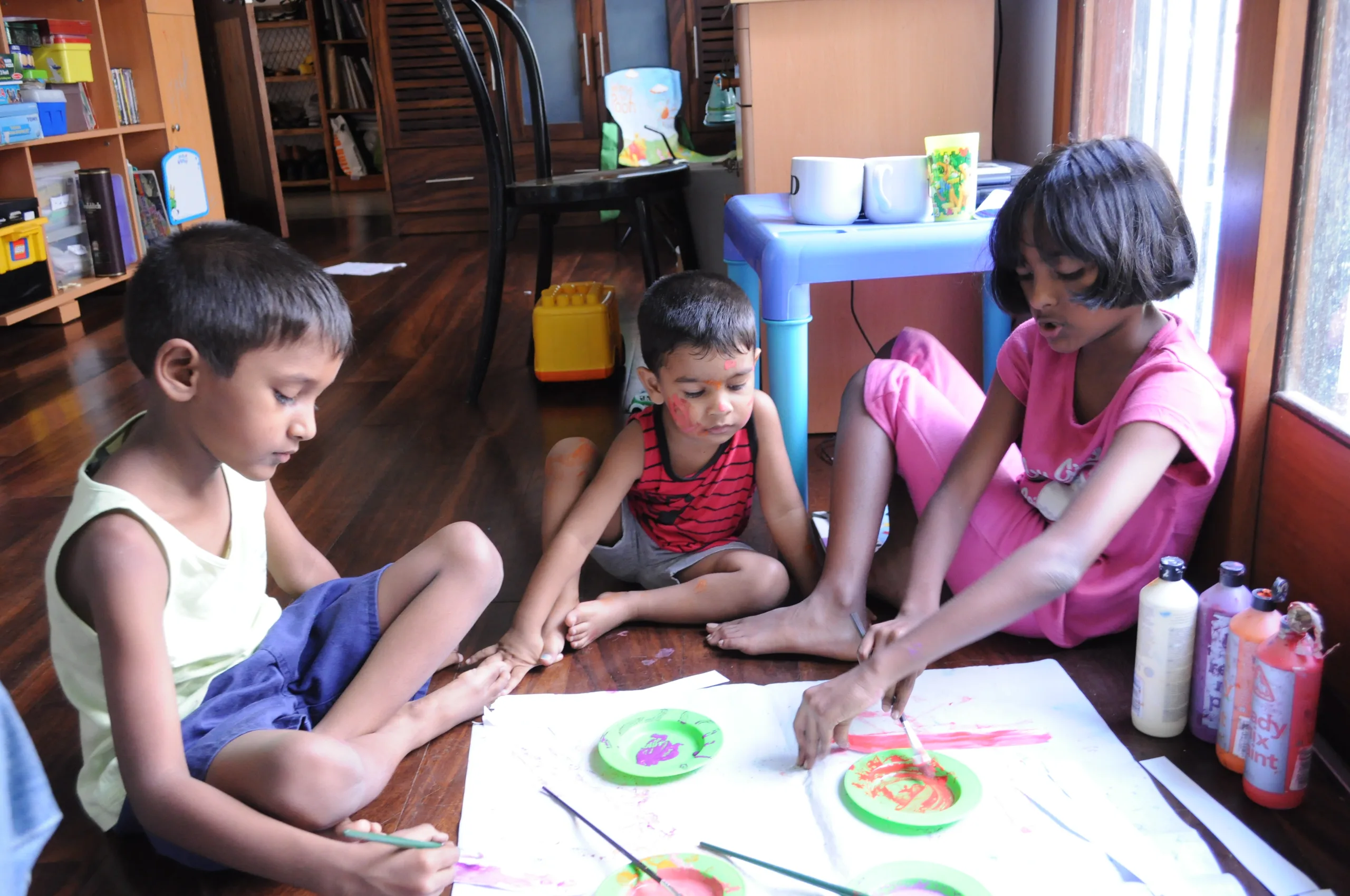 Three children painting together on the floor